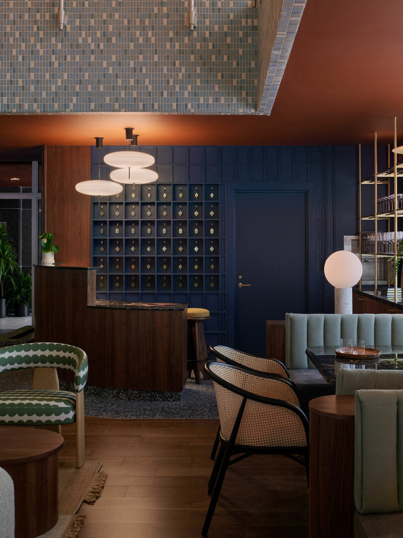 Modern hotel lobby at the Municipal Grand with patterned tile ceiling, dark wood furniture, blue wall cubbies, lounge chairs, and contemporary lighting.