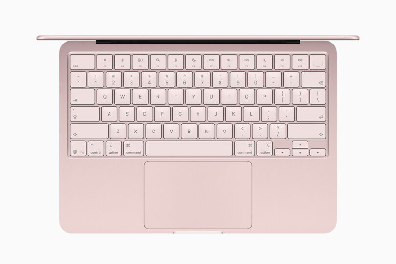 Una vista de una computadora portátil Apple rosa desde arriba, que muestra el teclado, el trackpad y parte de la bisagra de la pantalla.
