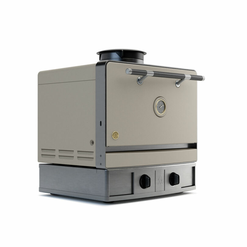 A beige Emberhaus metal oven with a front temperature gauge, two control knobs, and a chimney vent on top, set on a sturdy steel base.