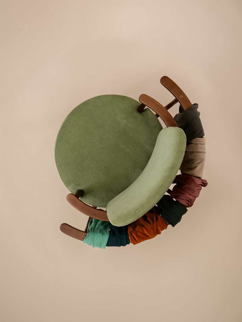 A green upholstered chair with wooden arms, viewed from above, with various colorful pieces of fabric draped over the front edge of the seat.