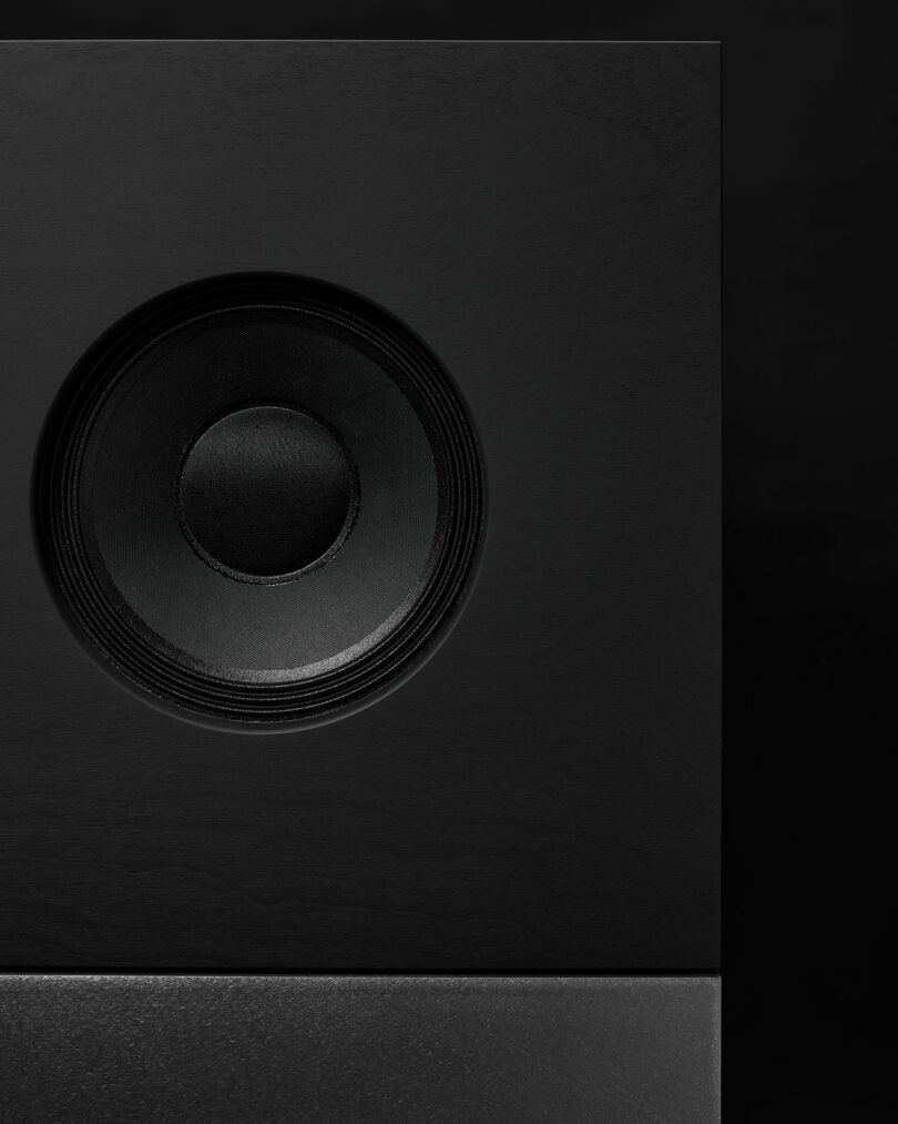 Close-up of a black speaker with a visible circular woofer on a dark background, highlighting the design as Studio D.A and Nocs debut the Braque stereo system.