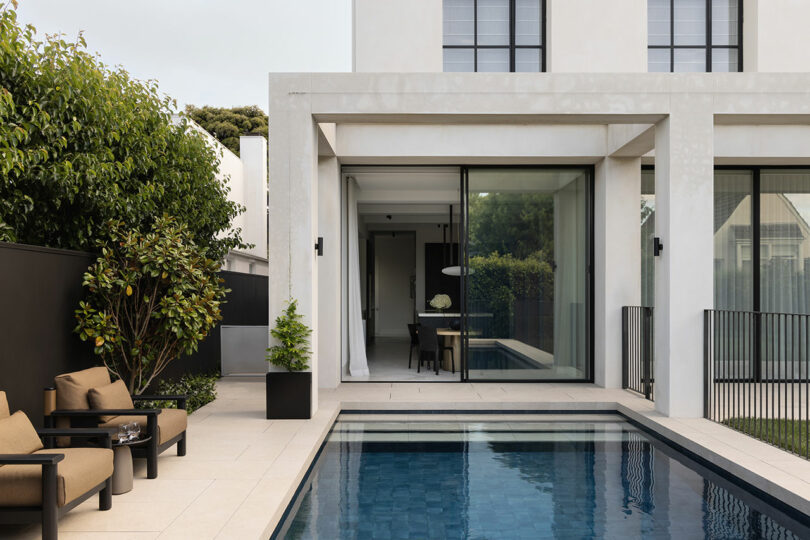 Modern house with large windows opens to a patio with a small rectangular pool, outdoor seating, potted plants, and minimalist landscaping.