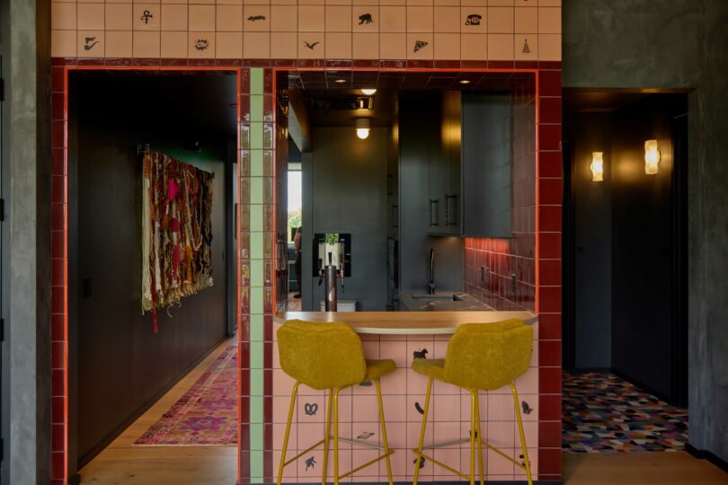 A modern Powell kitchen with a pink tiled breakfast bar, two yellow stools, dark cabinetry, and eclectic wall decor and flooring in the surrounding areas.
