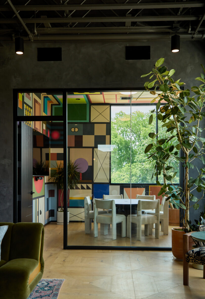 A modern glass-walled Powell meeting room with colorful geometric wall art, white chairs around a table, large windows, and indoor plants.
