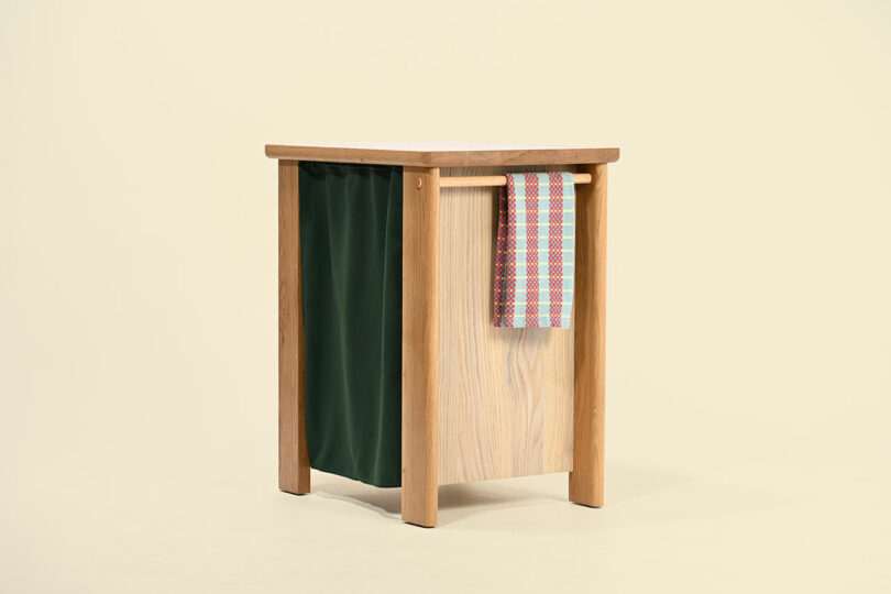 Una mesa auxiliar de madera con un bolsillo de tela verde en un lado y un trozo de tela a cuadros de colores que cuelga de la barra horizontal.