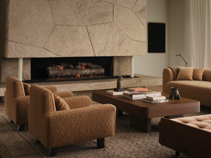 Modern living room with a large stone fireplace, beige armchairs, a matching sofa, and a wooden coffee table with books—an inviting space inspired by OSKLO’s signature neutral decor.