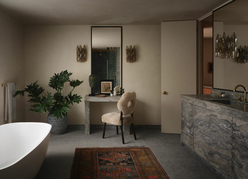 Modern bathroom with OSKLO-inspired touches: freestanding tub, large plant, marble vanity with chair, decorative mirror, and a patterned rug on the floor.