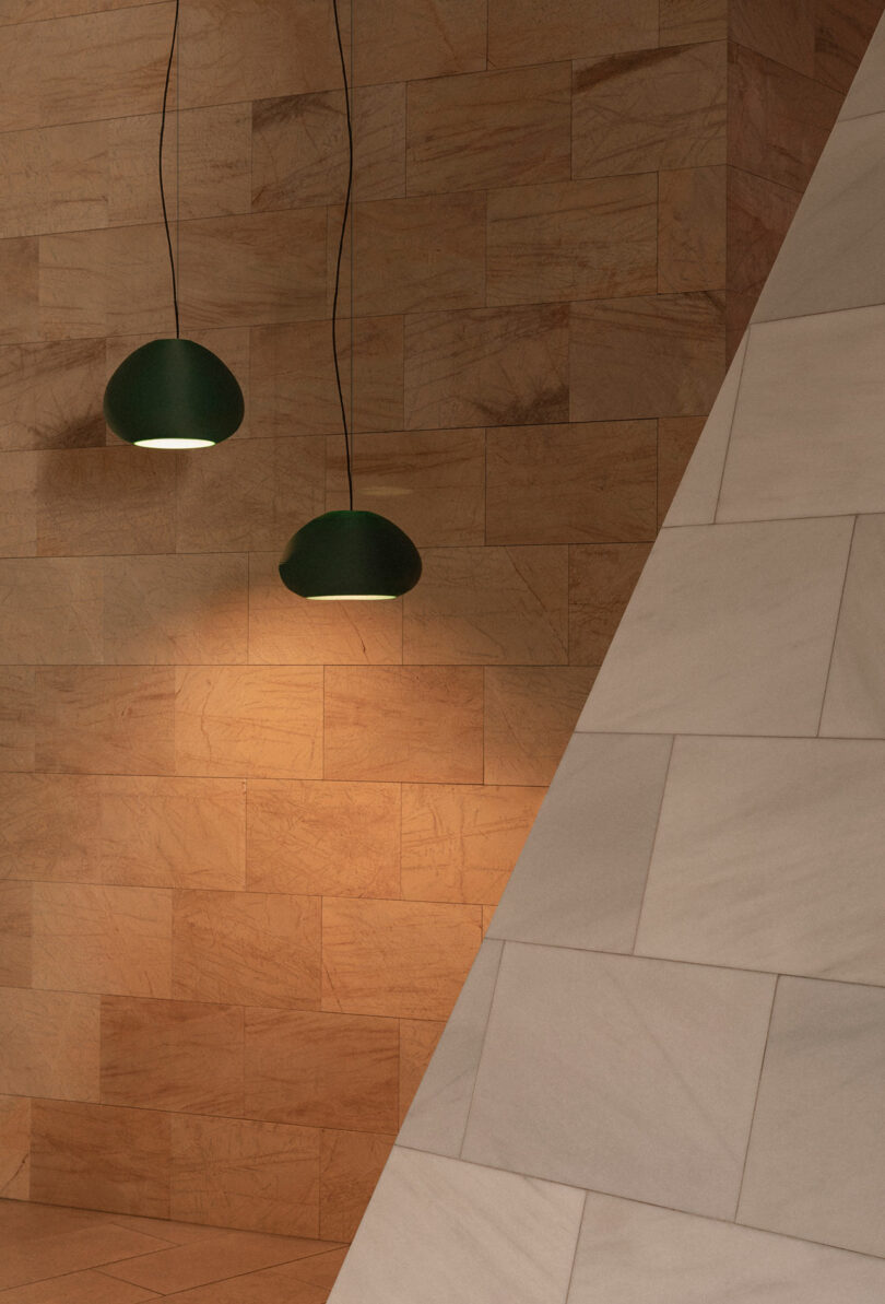 Two green pendant lights hang against a tan stone-tiled wall, with a large diagonal white-tiled structure in the foreground.