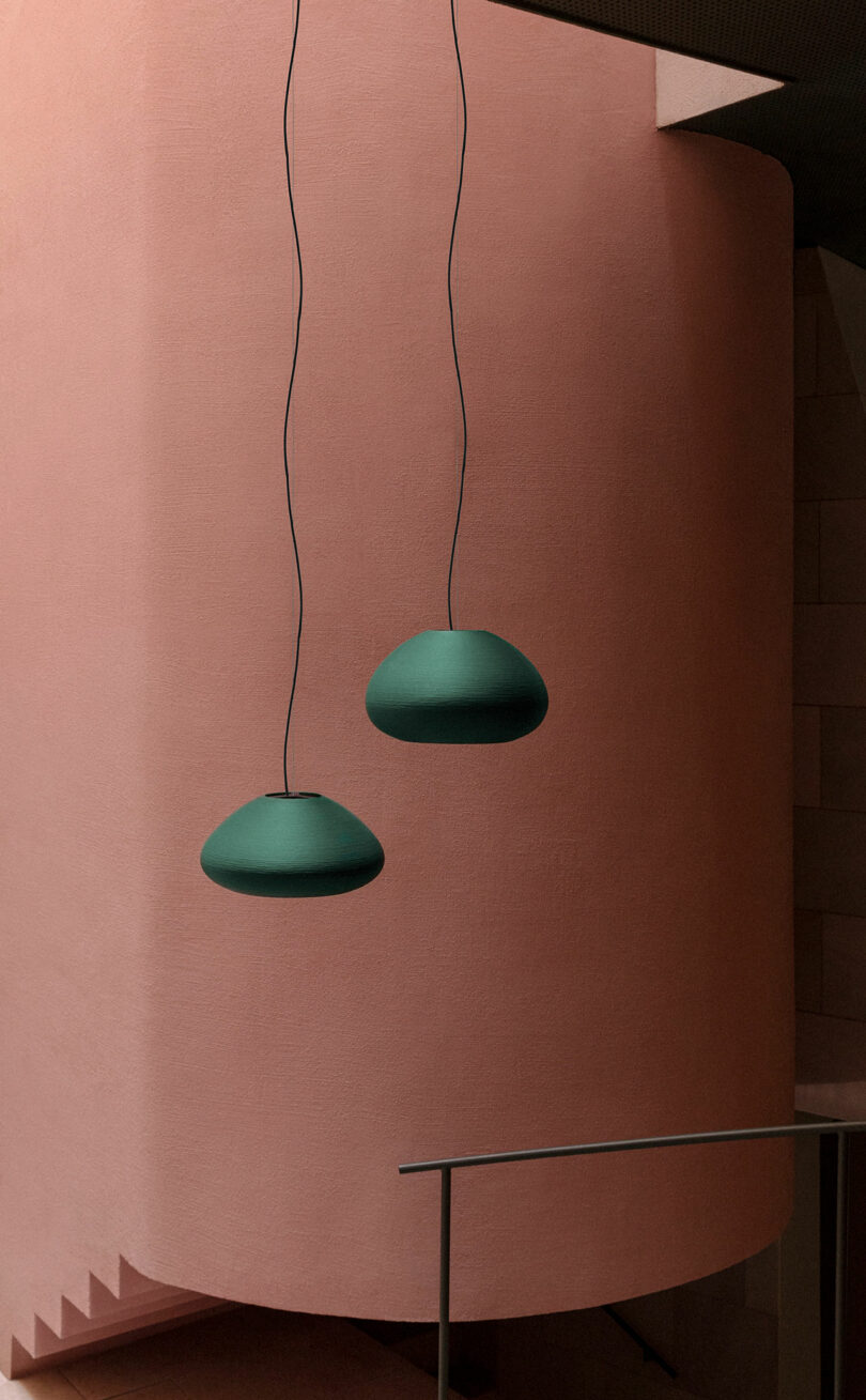Two green pendant lights hang in front of a curved, pink-textured wall with a staircase and metal railing partially visible.