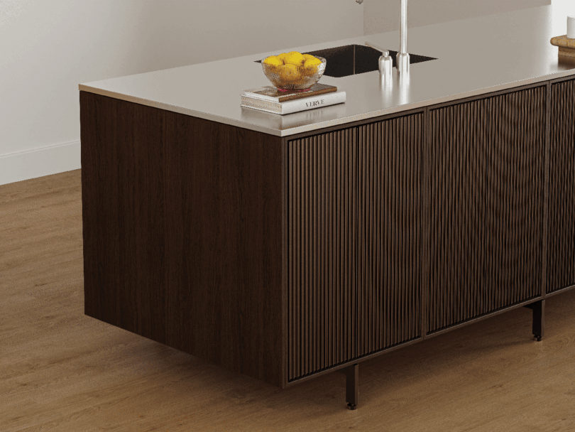 La moderna isla de cocina Vipp se asienta elegantemente sobre el suelo de madera y cuenta con una base de madera, una encimera blanca, libros, un vaso de agua y un grifo blanco.