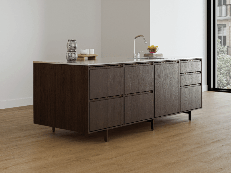 Isla de cocina moderna con armarios de madera oscura, fregadero Vipp y algunos elementos sobre la encimera en una luminosa estancia minimalista con suelo de madera clara.