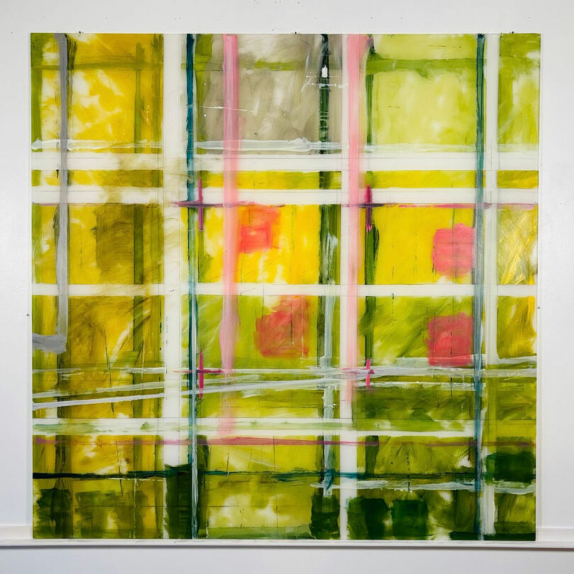 Abstract painting by Barry Ginder featuring intersecting vertical and horizontal lines in yellow, green, white, pink, and red tones, with a grid-like pattern on a square canvas against a white wall.