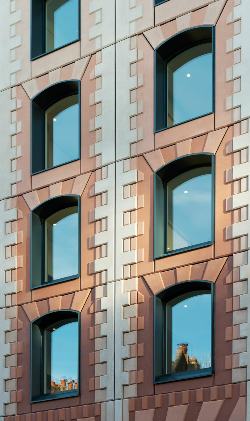 Close-up of a building facade featuring rows of large arched windows set in a pinkish-tan patterned exterior with geometric detailing.