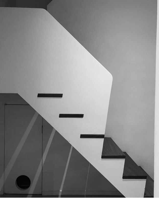 Minimalist black and white photo of a staircase with geometric lines, wooden steps, and a small door under the stairs—perfect for this week's Friday 5 architectural highlights.