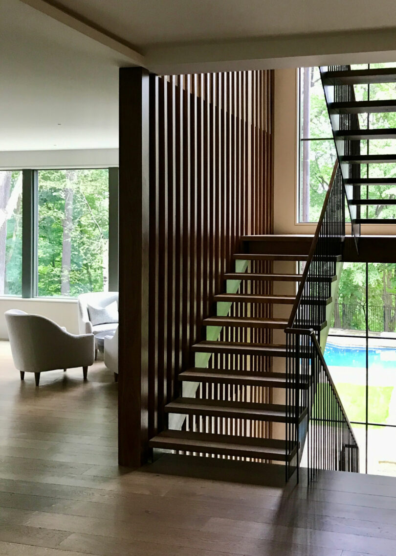 Modern staircase with wooden slats and glass panels highlights this Friday 5 feature; large windows reveal lush outdoor greenery and a sparkling swimming pool in a bright living space.