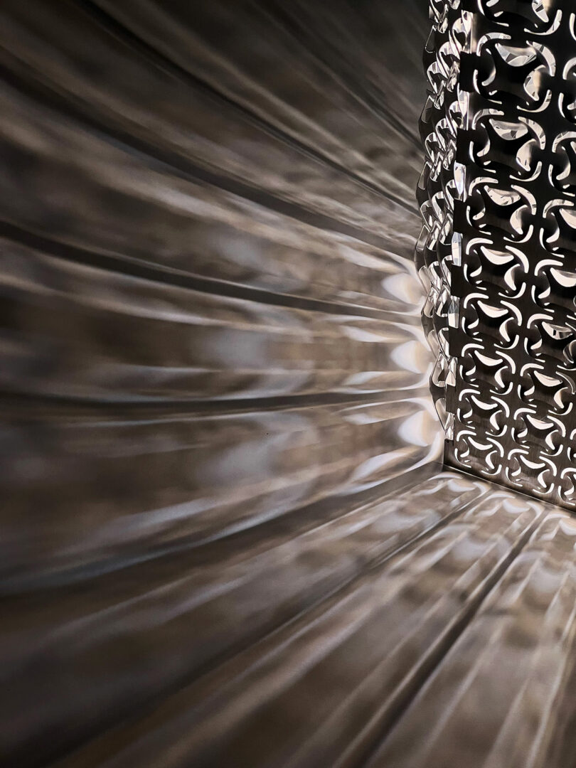 A close-up of a decorative metal lamp casting patterned light and shadow on a nearby wall and surface.