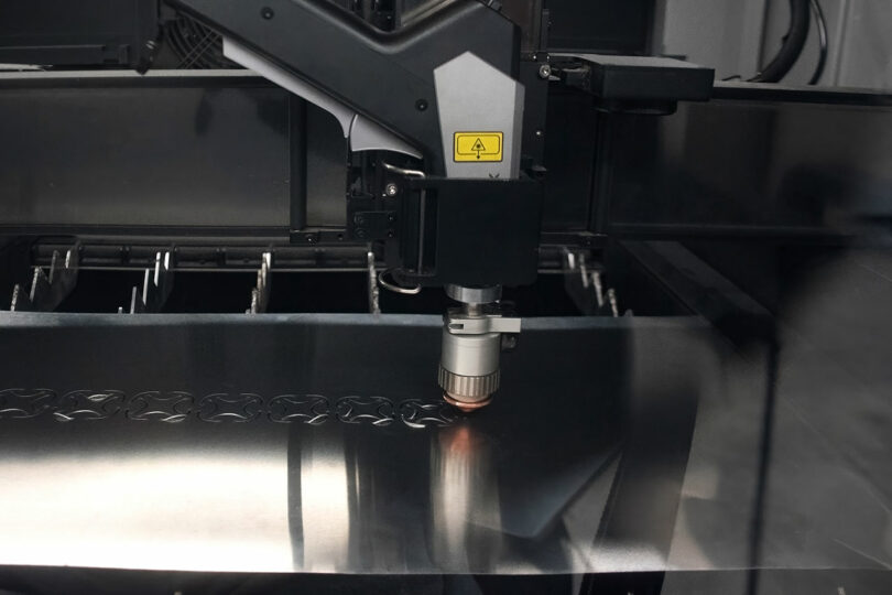 A CNC laser cutting machine cuts intricate patterns into a sheet of metal in an industrial setting.