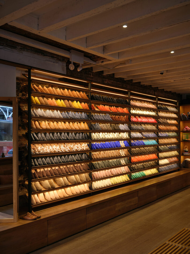 A wall display of neatly arranged shoes in various colors and styles inside a well-lit retail store with wooden accents.