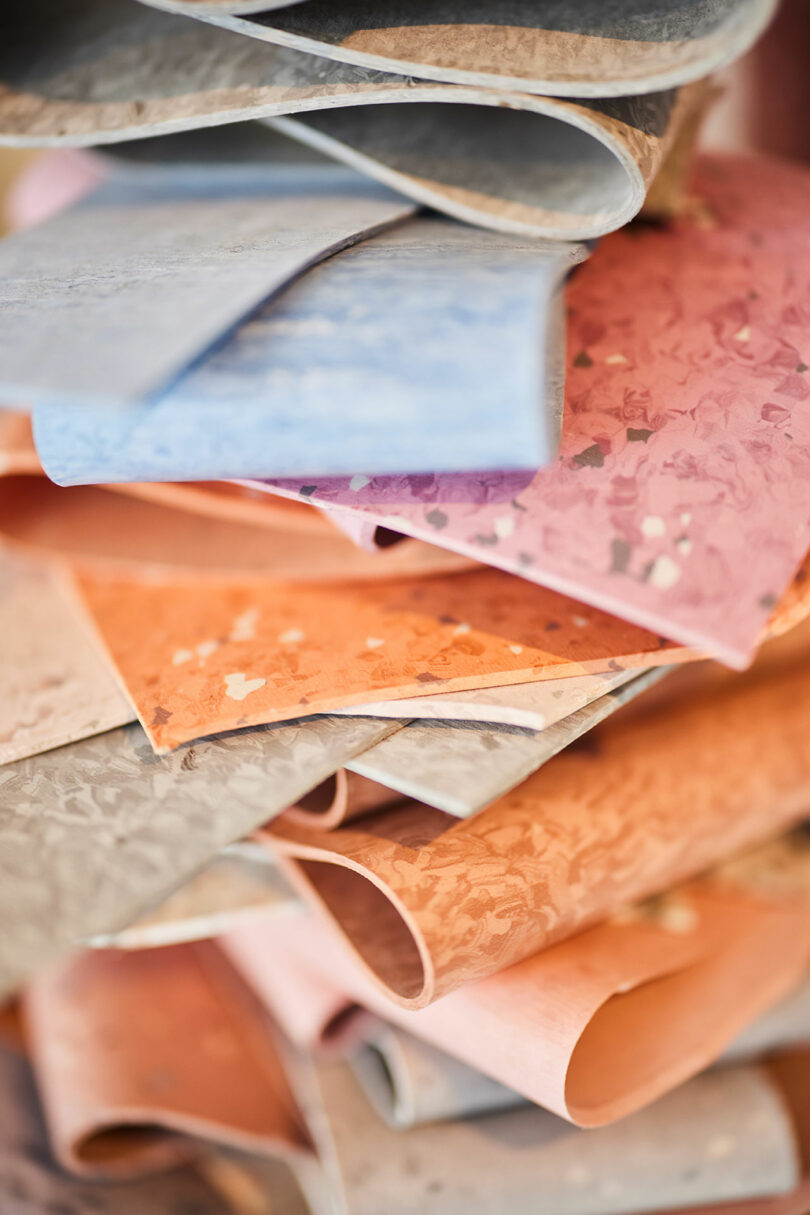 A close-up of stacked, colorful textured paper sheets in shades of blue, pink, orange, and gray—some with marbled or speckled patterns—evokes the vibrant design versatility found in Tarkett collections.