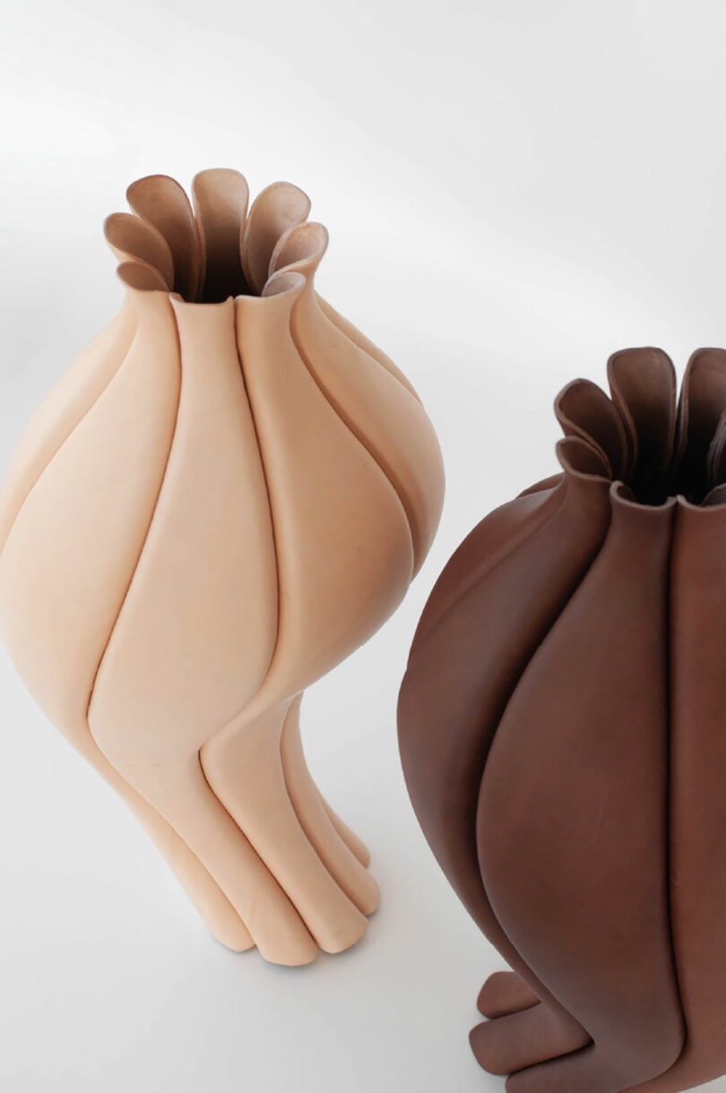 Two sculptural vases, one light beige and one dark brown, feature folded, petal-like shapes and stand upright on a white surface.