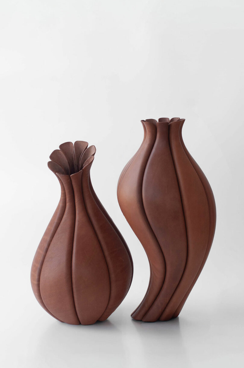 Two sculptural brown vases with curved, petal-like designs stand on a light surface against a plain white background.