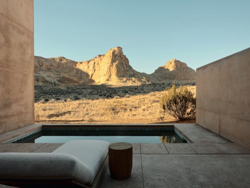 A plunge pool and a lounger on a concrete terrace overlook a sunny desert landscape of rocky hills under a clear sky.