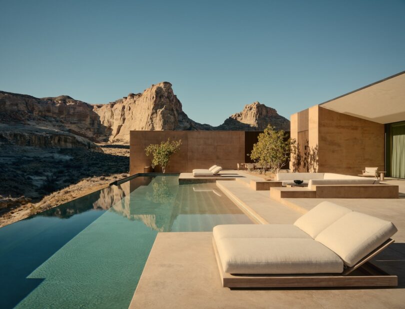 Modern villa with an infinity pool and sunbeds and a view of a rocky desert landscape with large rocks under a clear blue sky.