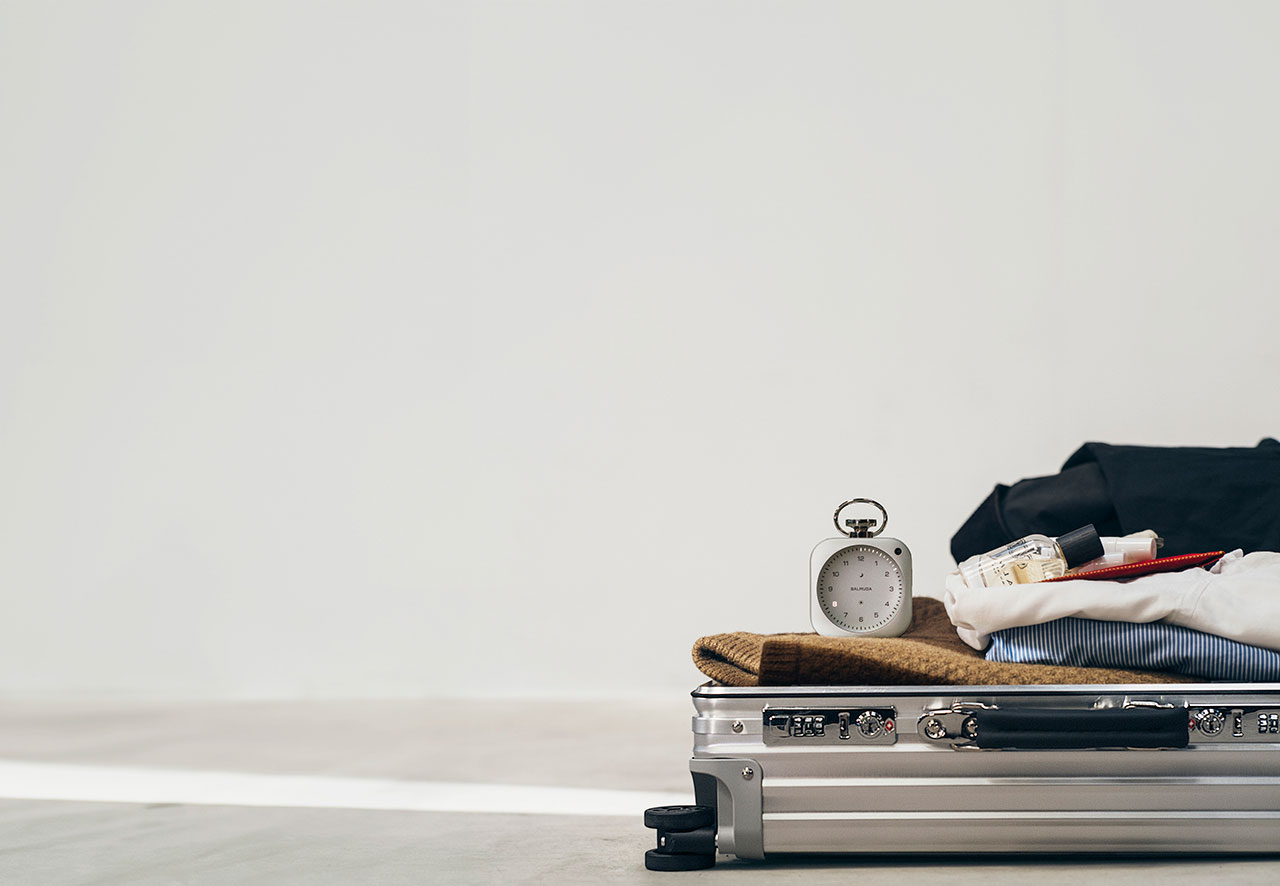 A suitcase lies open on the floor with neatly folded clothes, toiletries, and a small analog clock placed on top.