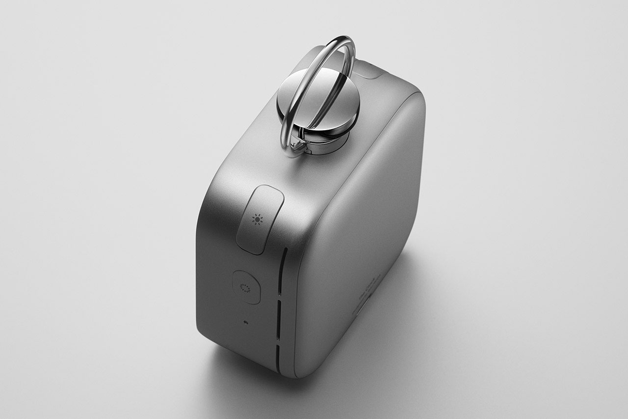 A compact, rectangular metallic device with rounded edges, featuring a prominent circular dial and a button on its top surface.