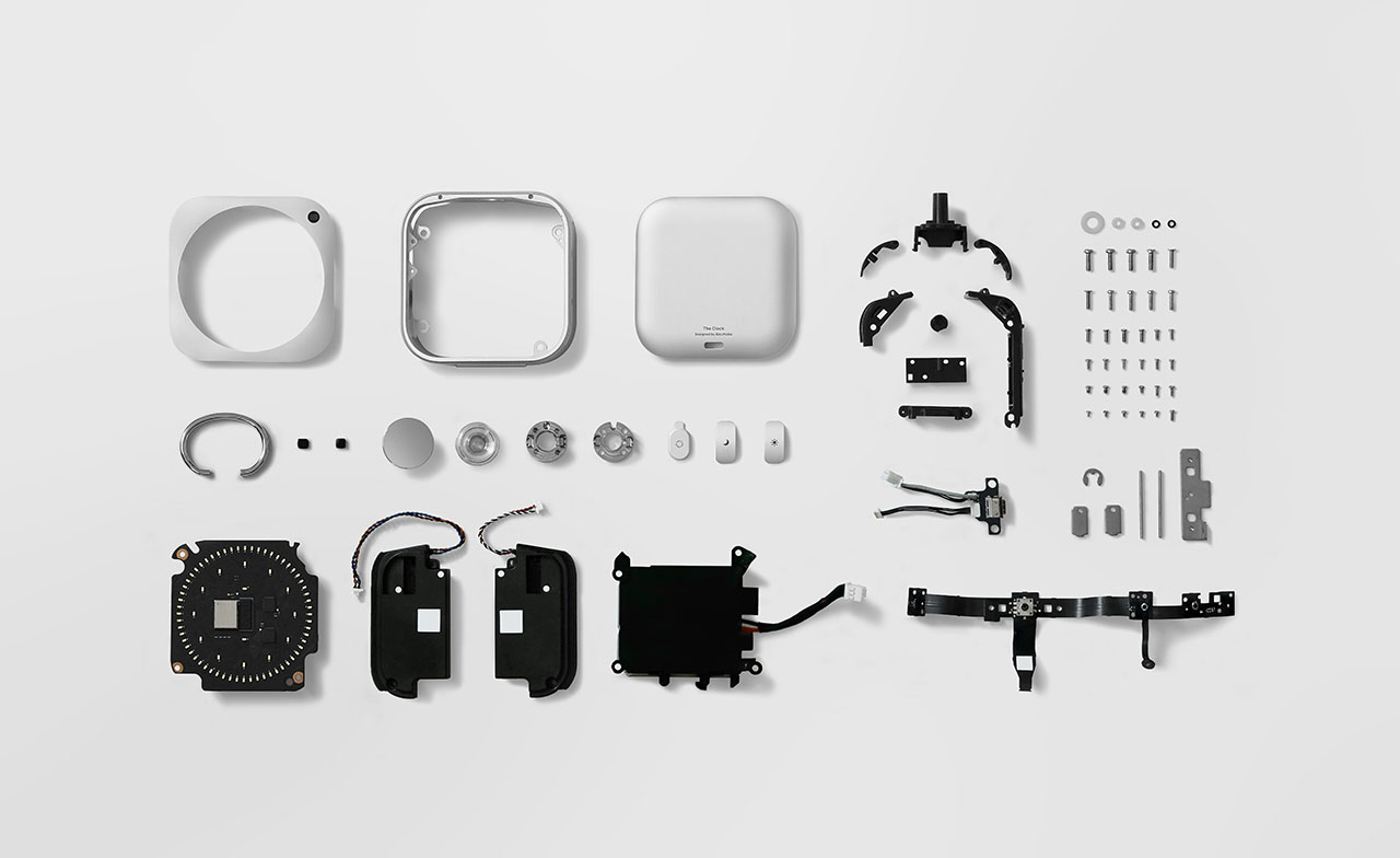 Disassembled electronic device with its components, including wires, screws, circuit boards, and casing parts, arranged neatly on a white background.