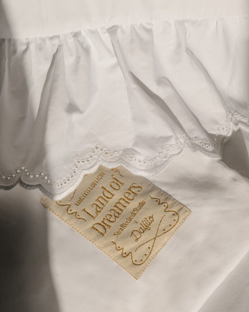 A white ruffled fabric with eyelet trim is draped above a beige embroidered label reading "Land of Dreamers, Limited Edition, Sanluca Studio, Dalica," evoking the whimsy of balloon installations.
