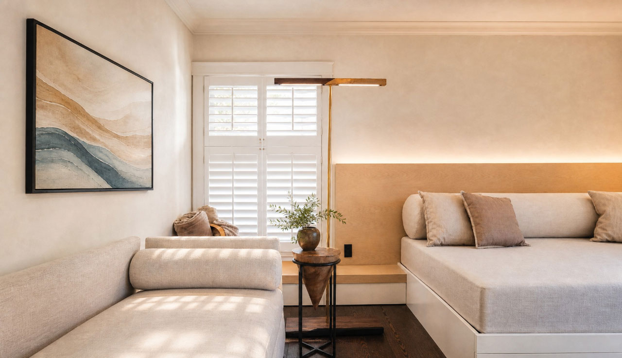 A minimalist living room with two beige sofas, a round side table with a plant, a floor lamp, wall art, and shuttered windows allowing natural light in—perfect inspiration for this week’s Friday Five.