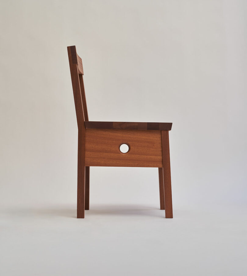 Wooden chair with a square seat, straight backrest, and a circular hole in the center of the seat's side panel, shown against a plain light background.