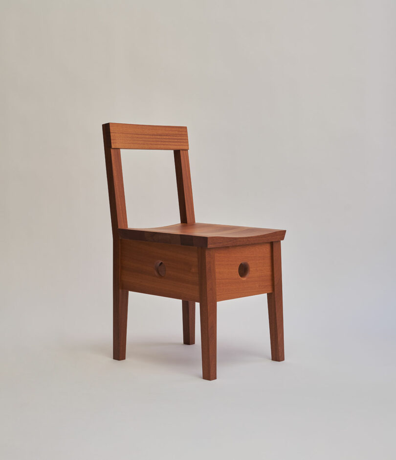 A wooden chair with a square seat, a straight backrest, and a built-in drawer under the seat, set against a plain light background.