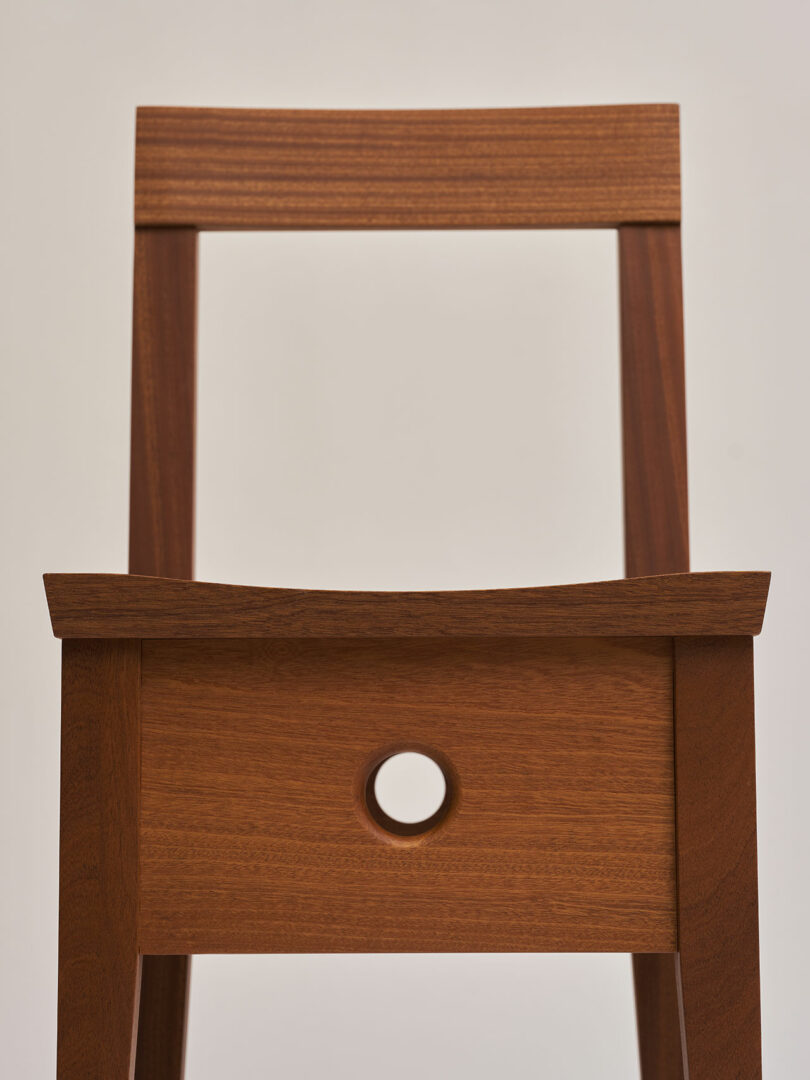 A wooden chair with a minimalist design, featuring a rectangular backrest and a circular cut-out in the center of the seat.