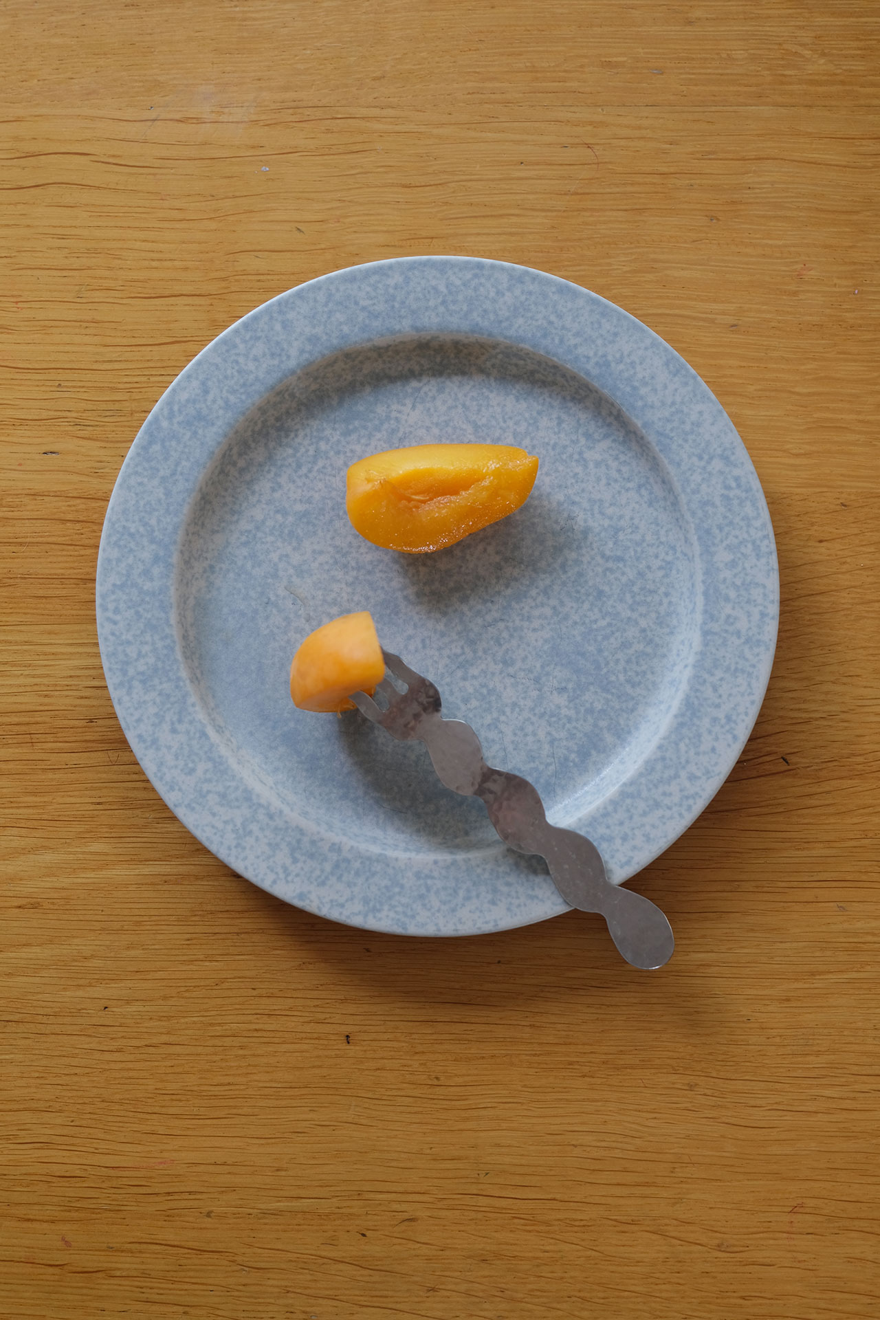 A blue speckled plate with a metal utensil holding a small orange fruit segment, and another orange fruit segment on the plateâeach piece a vibrant building block of color and flavor.