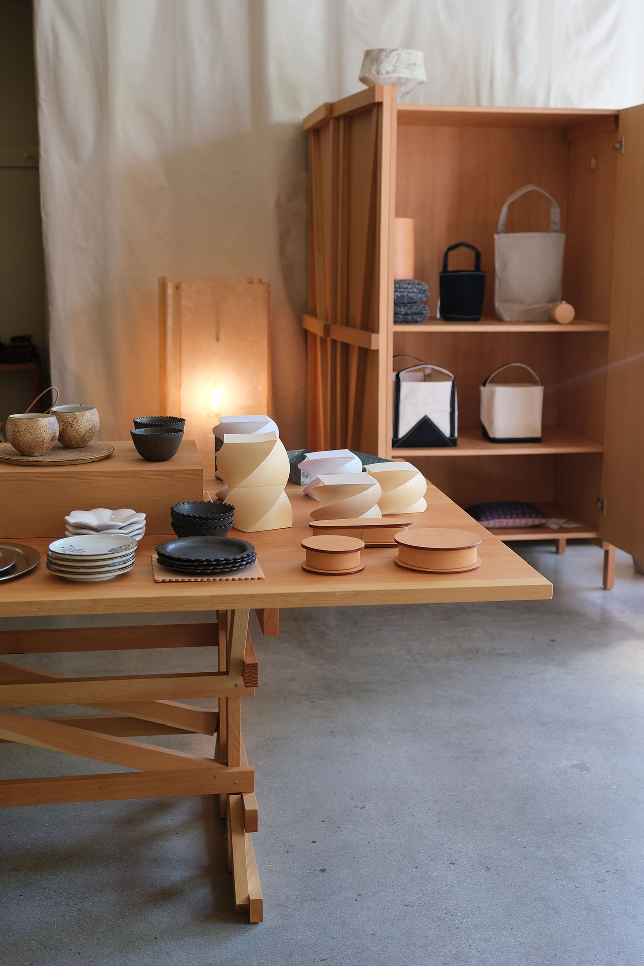 A wooden table and open cabinet display ceramic bowls, plates, and basketsâeach piece a building block of minimalist decorâin a room with neutral tones and soft lighting.