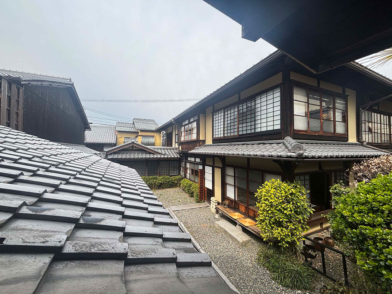 Traditional Japanese house with tiled roofs, wooden frames, and large windows, surrounded by greenery on a cloudy day—a serene setting reminiscent of Kawai Kanjira’s architectural inspirations.