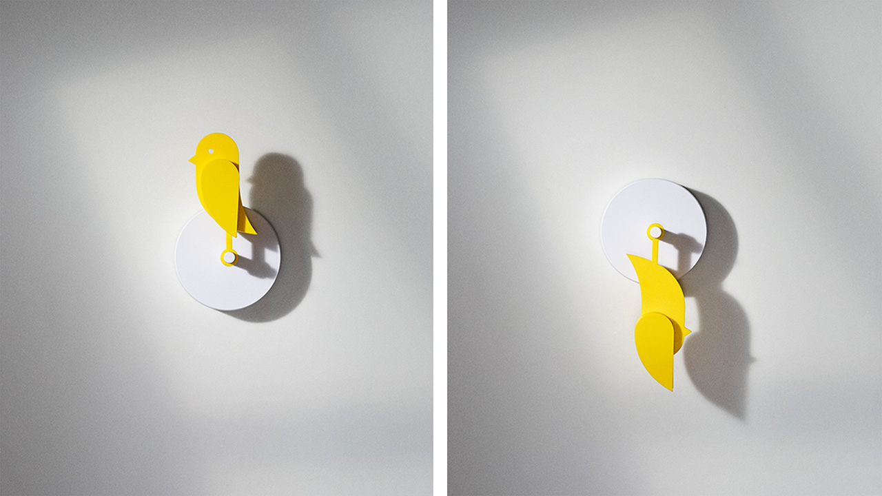 Dos modernos relojes de pared con superficies blancas y motivos esculturales amarillos; un reloj se parece a un pájaro, mientras que el otro reorganiza creativamente las partes del cuerpo del pájaro verticalmente.