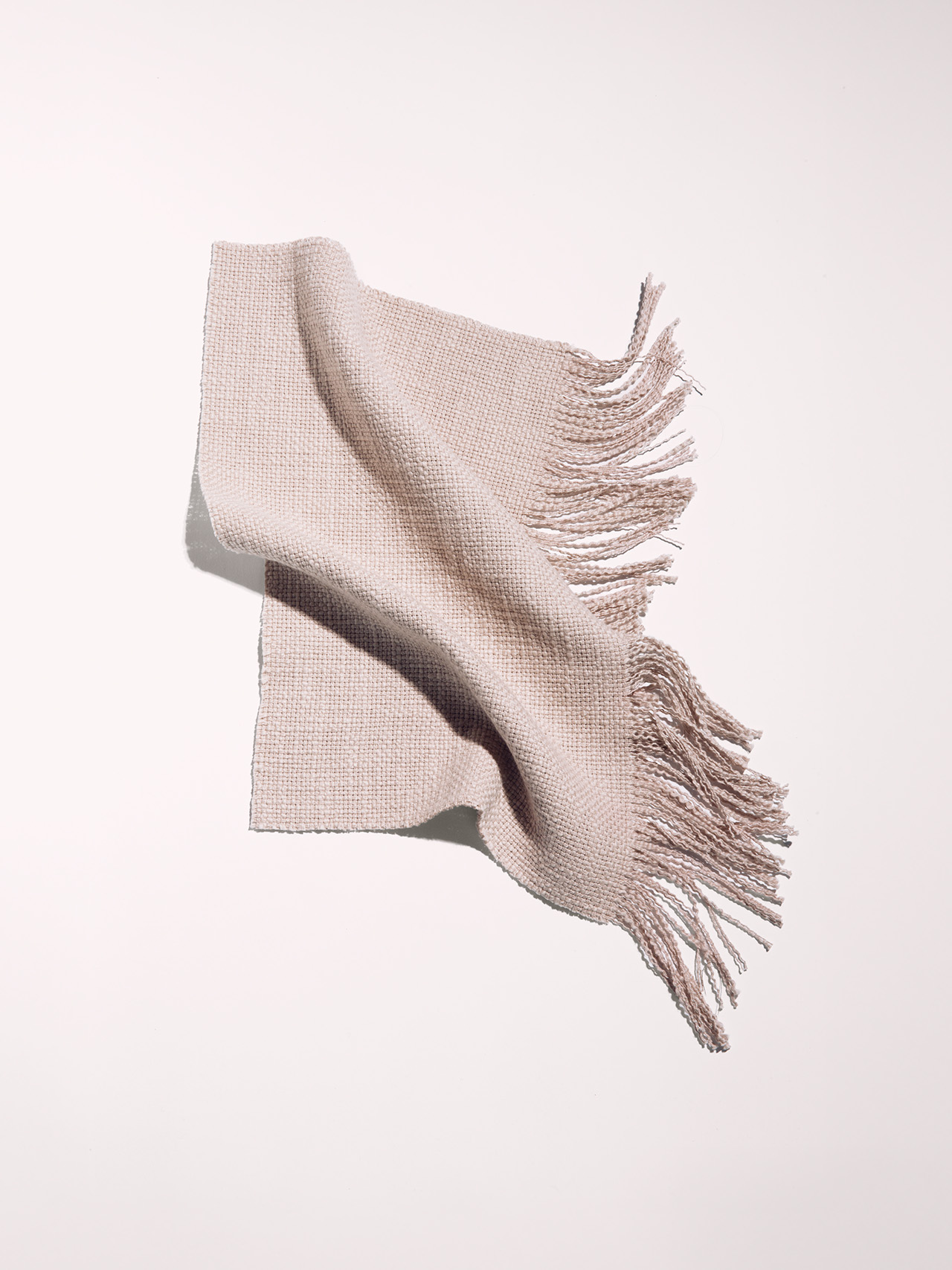 A light beige woven scarf with fringe on the ends, laid flat against a white background.