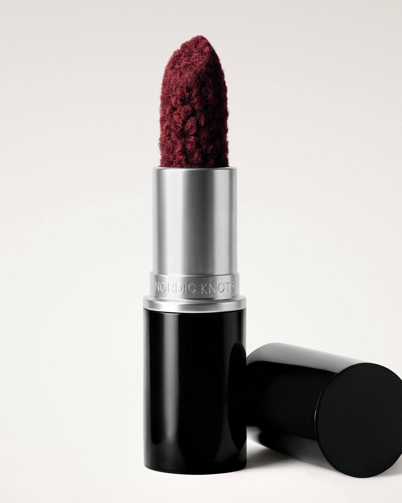 Un tubo de lápiz labial con forma de hilo o tejido texturizado de color rojo oscuro que se mantiene en posición vertical con la gorra al lado.
