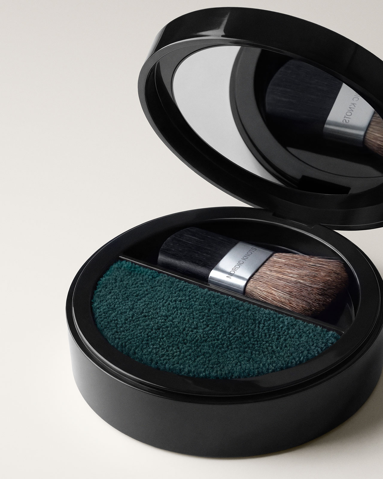 Compacto redondo negro con espejo, pequeña brocha de maquillaje plana con polvo texturizado verde y cerdas marrones.