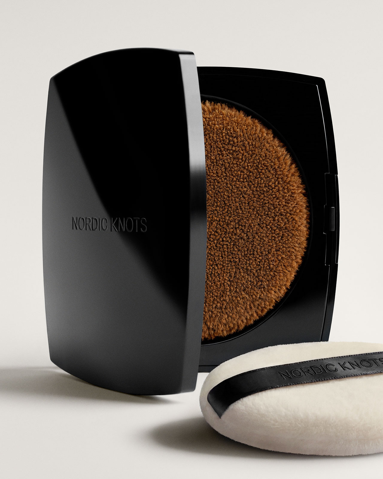 Una caja negra compacta etiquetada "nudo nórdico" El interior tiene un acabado texturizado marrón y presenta una almohadilla aplicadora blanca con rayas negras y la marca a juego.