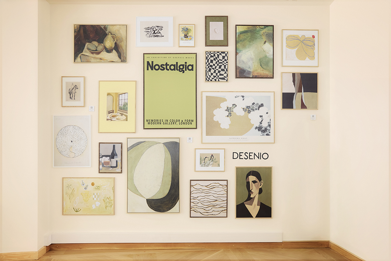 A gallery wall with assorted framed art prints and paintings of various sizes, styles, and colors, displayed on a cream-colored wall with a wooden floor—an inspiring showcase for any dgert Comms creative space.