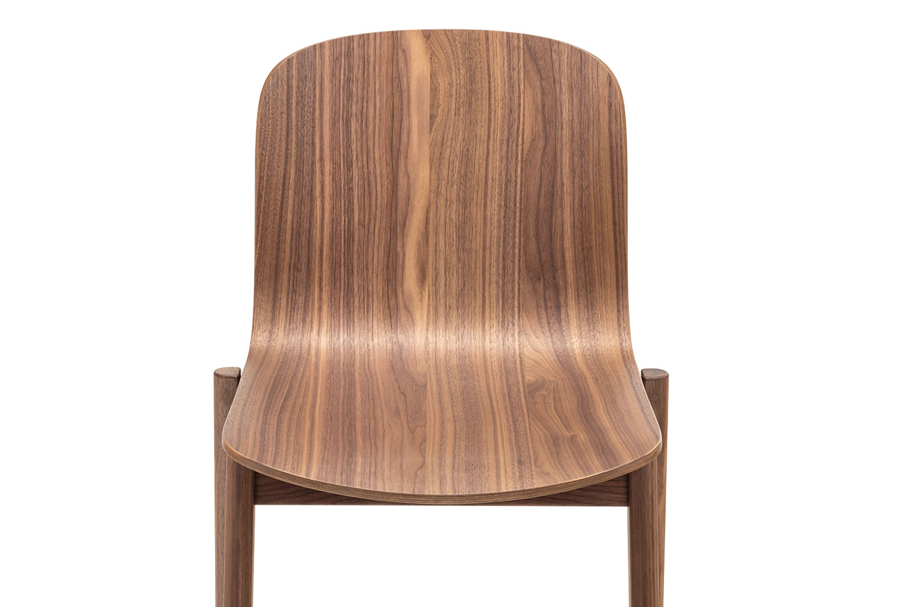 Vista frontal de una silla de madera sencilla y moderna de Alexander Gufler con asiento y respaldo curvos con un patrón de vetas de madera natural.