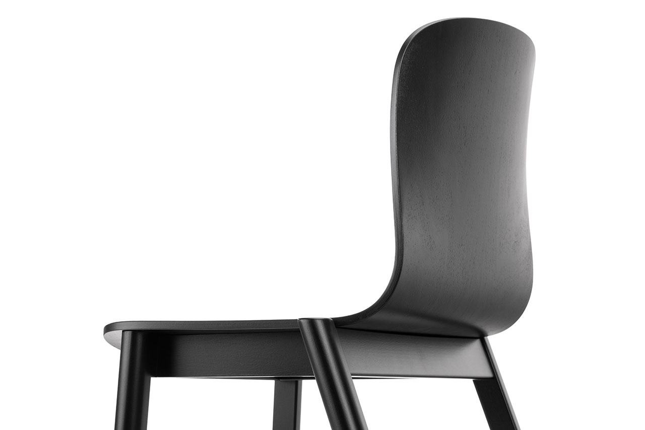Vista cercana de la moderna silla de madera negra de Alexander Gufler que muestra el respaldo curvo y el asiento desde un ángulo bajo sobre fondo blanco.