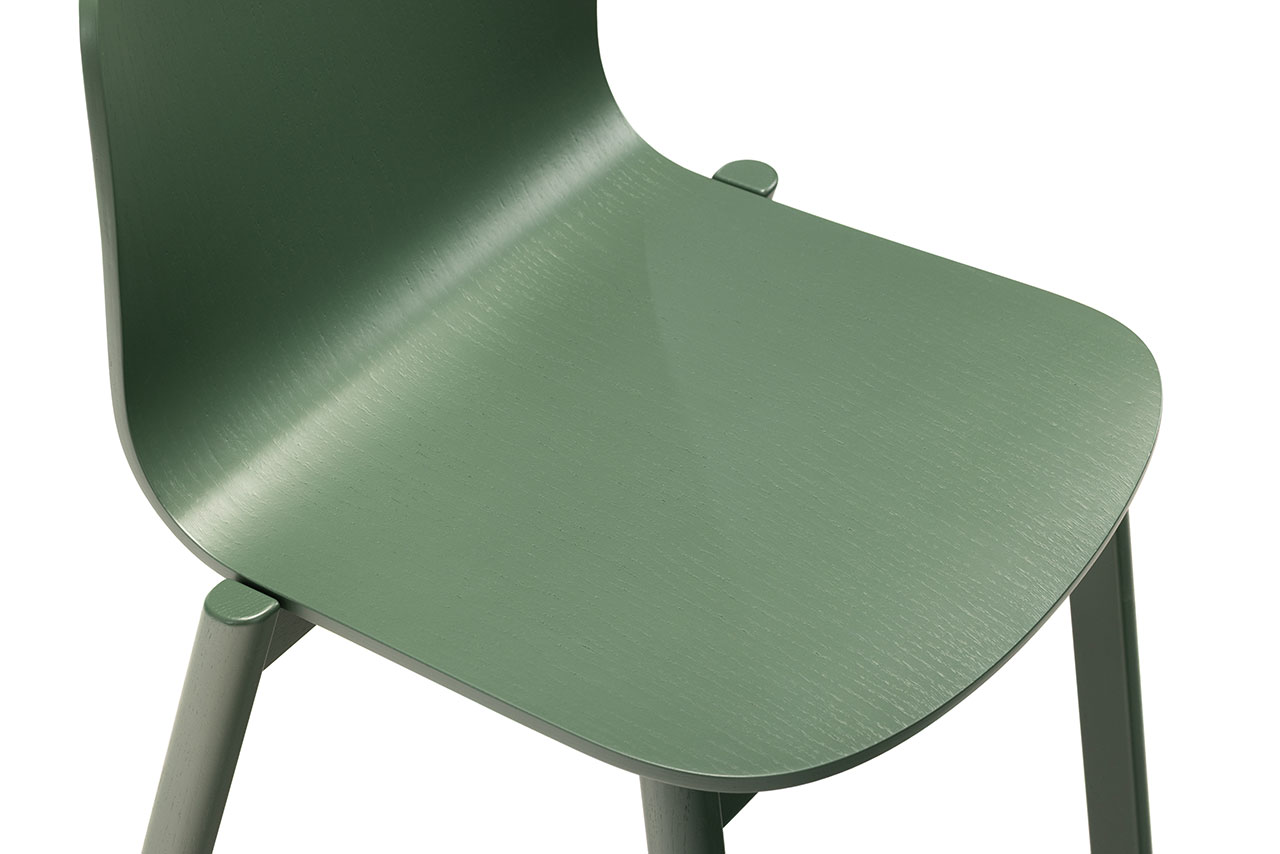 Vista cercana de una silla de madera verde de Alexander Gufler, que muestra el asiento liso, parte del respaldo y las patas sobre fondo blanco.