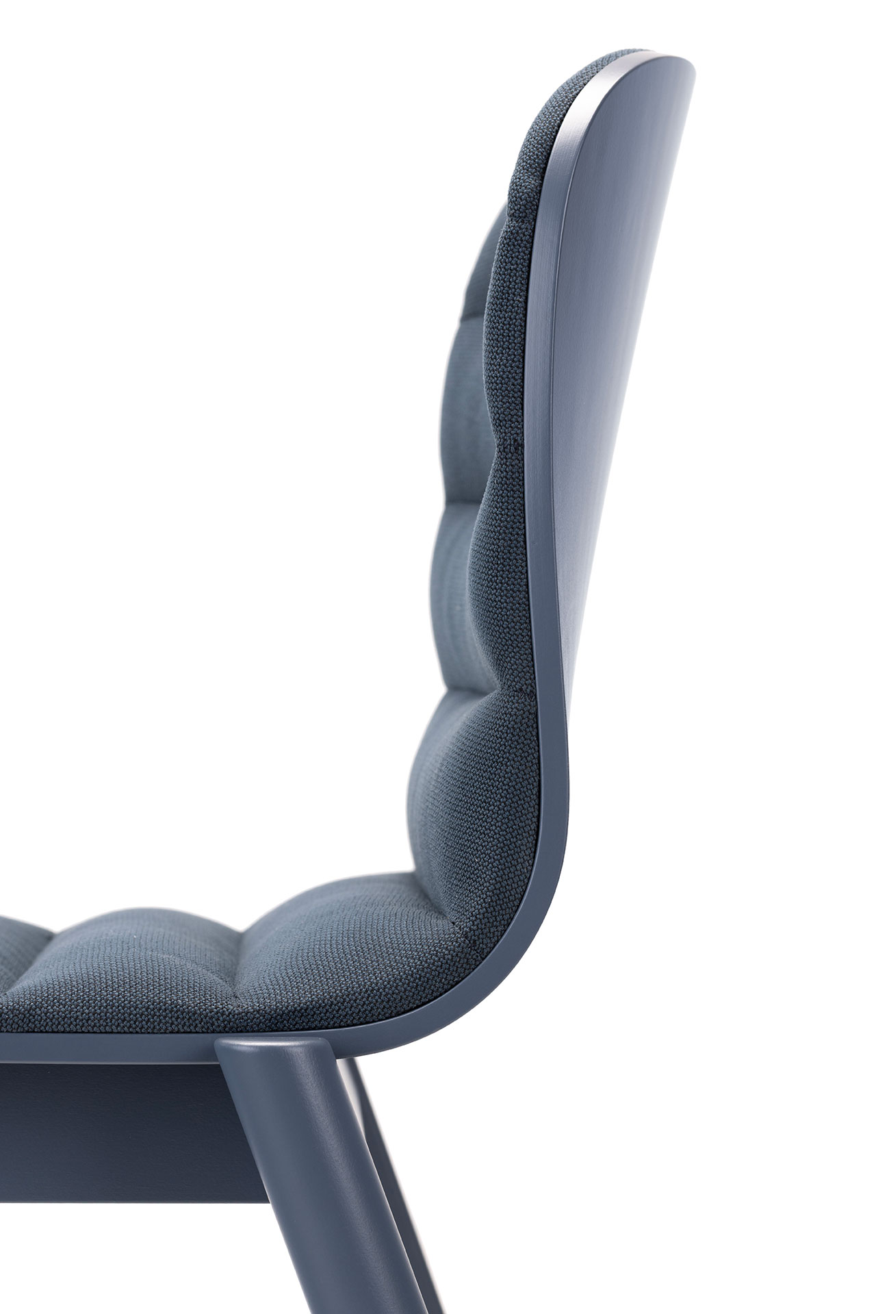 Vista lateral en primer plano de una silla moderna diseñada por Alexander Gufler con tapizado azul, respaldo y asiento tapizados y patas de color azul brillante sobre fondo blanco.