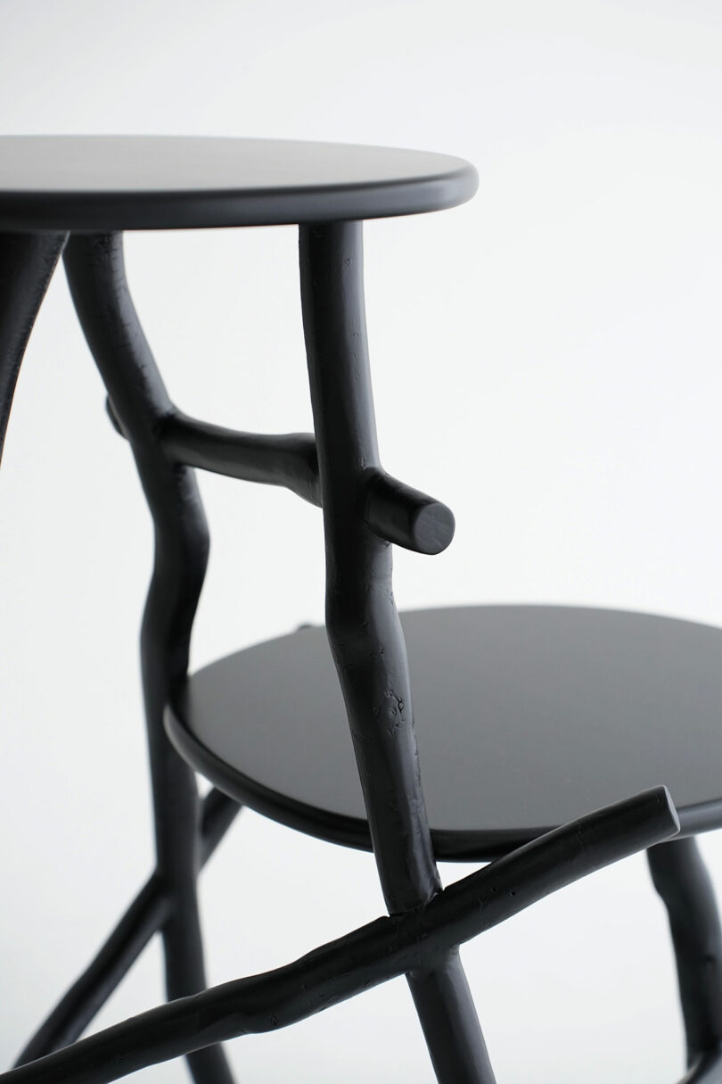 Close-up of a modern black chair with a round seat and irregular, branch-like legs and supports, set against a plain white background.