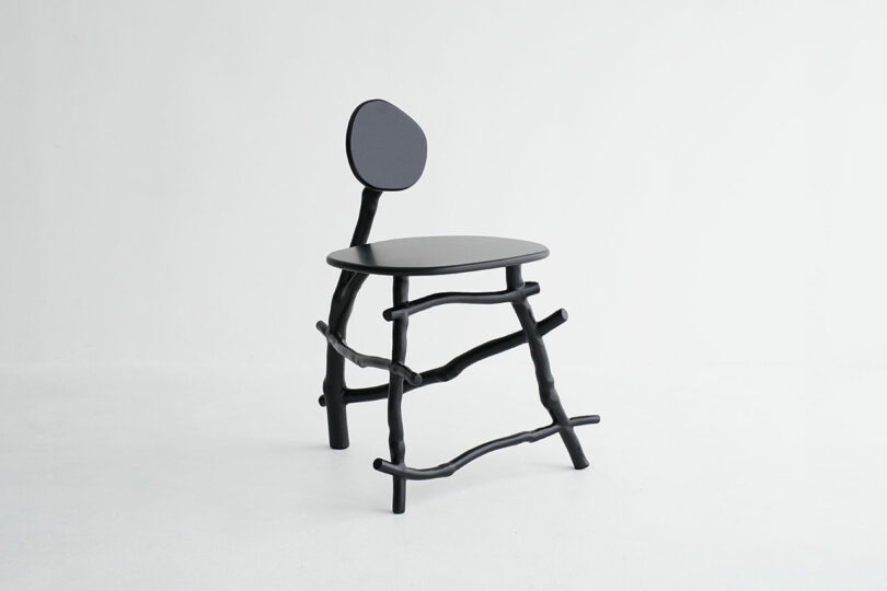 A modern black chair with a round seat, irregular stick-like legs, and an asymmetrical round backrest, set against a plain white background.